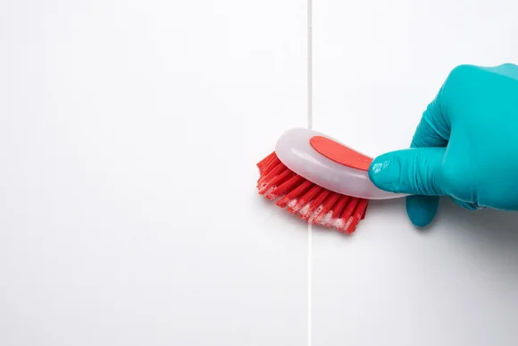 Hand in Gummihandschuh reinigt Fliesen